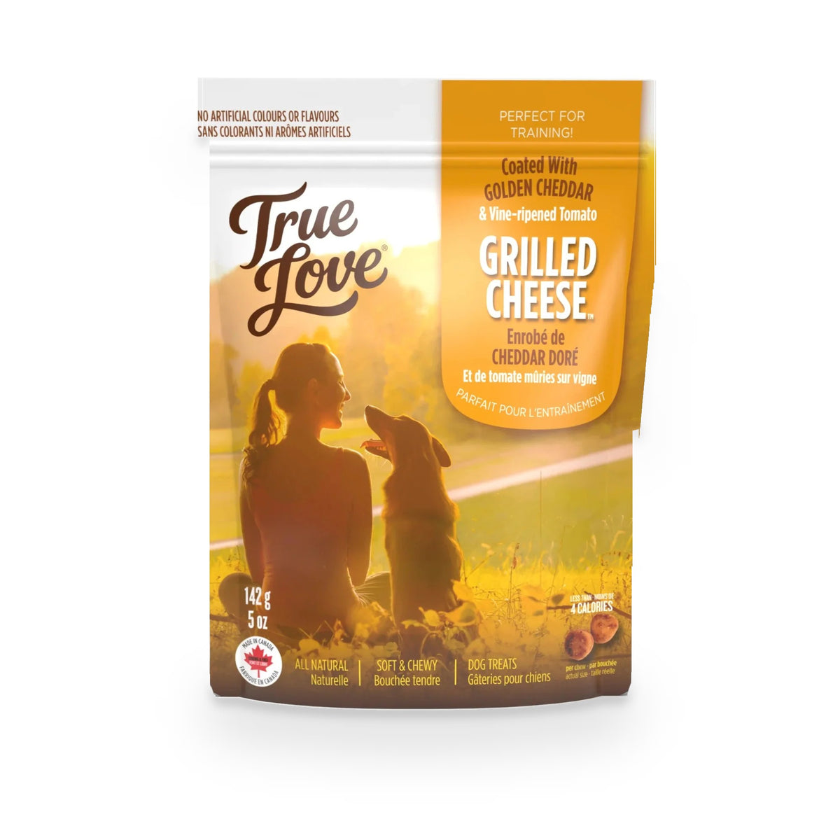Bag of True Love dog treats with a woman smiling at her dog on the grass. Grilled Cheese flavour - golden cheddar and vine-ripened tomato.